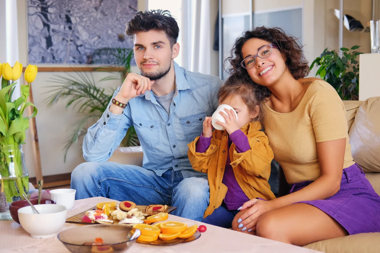 attractive-brunette-female-eyeglasses-bearded-stylish-male-their-cute-little-daughter-sits-couch-eat-lunch-living-room